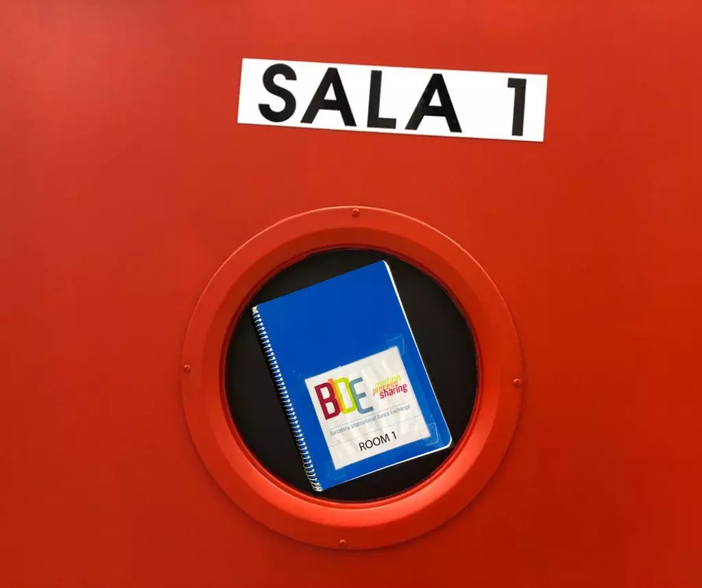 Blue notebook in round window of red door "Sala 1"